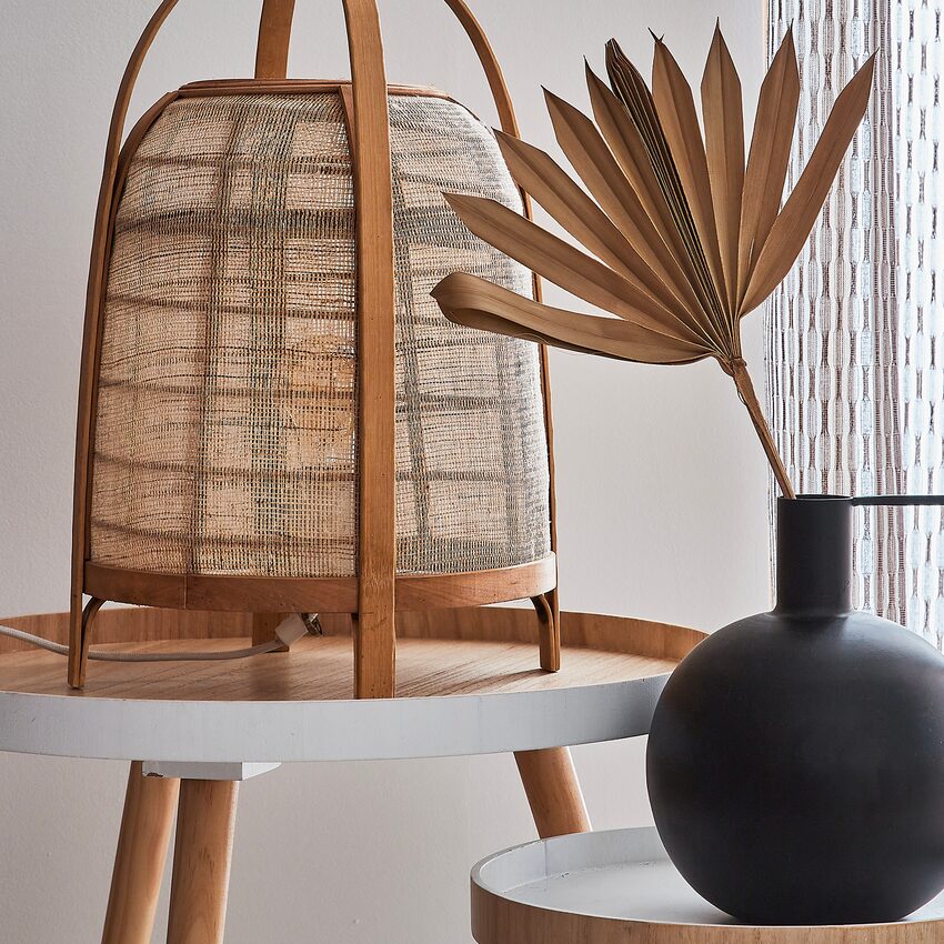 Lampe à poser en fibres naturelles et vase noir rond, posés sur deux petites tables basses
