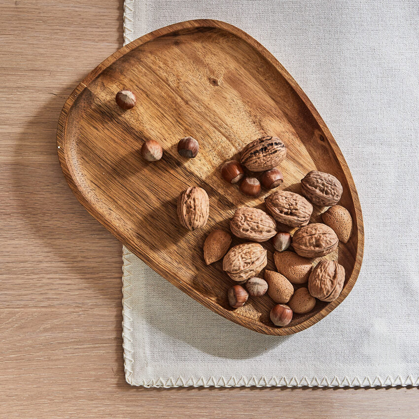 Un plateau en bois rempli de noix et noisettes est posé sur une nappe blanche