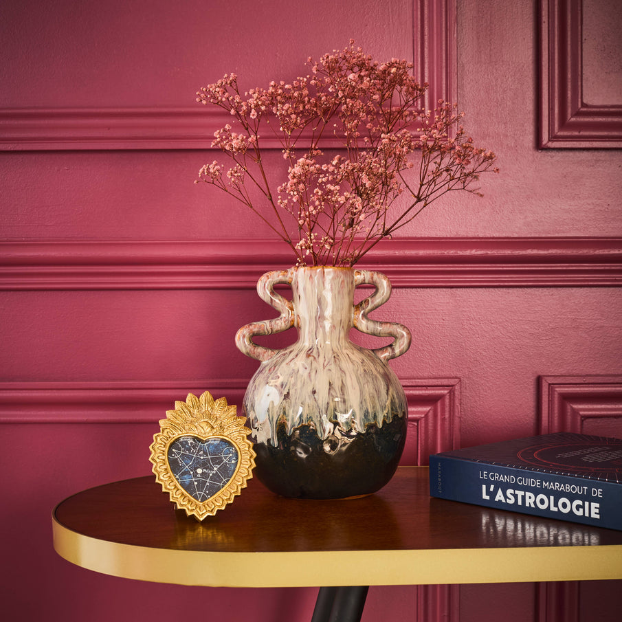 Vase posé sur une console en bois avec bordure dorée devant un mur peint en rose rouge