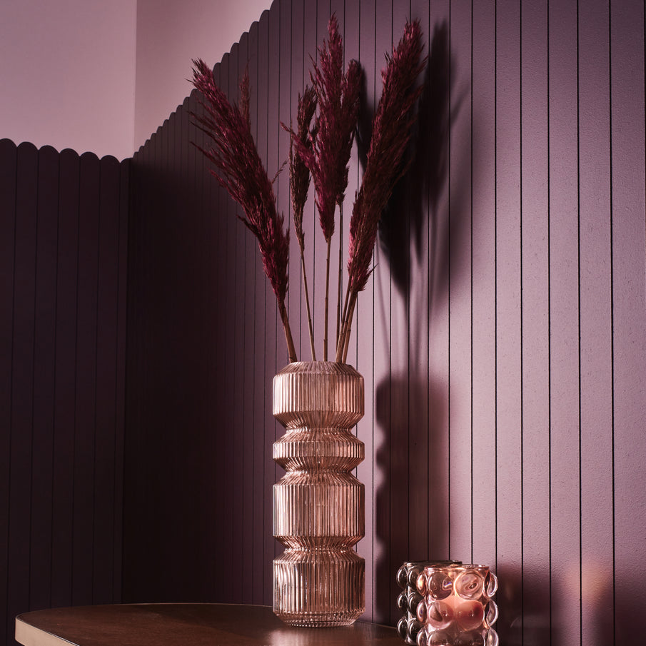 Vase en verre rose avec pampa séchée devant mur violet