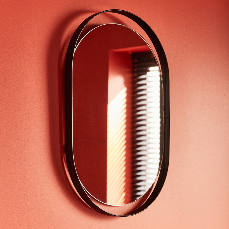 Miroir ovale au cadre métallique noir accroché à un mur rouge orange