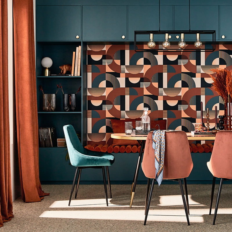 Salle à manger aux couleurs rouille et bleu paon avec chaises en velours et papier peint motif géométrique
