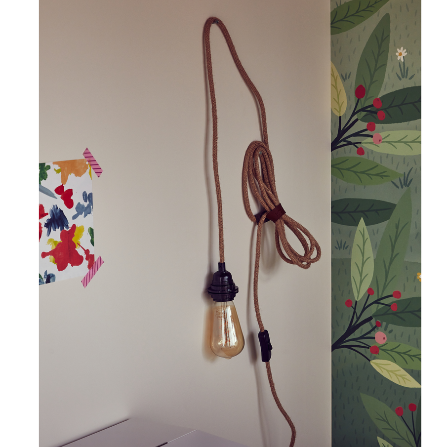 Sur un mur blanc, une ampoule pend le long d'une corde accrochée à un clou