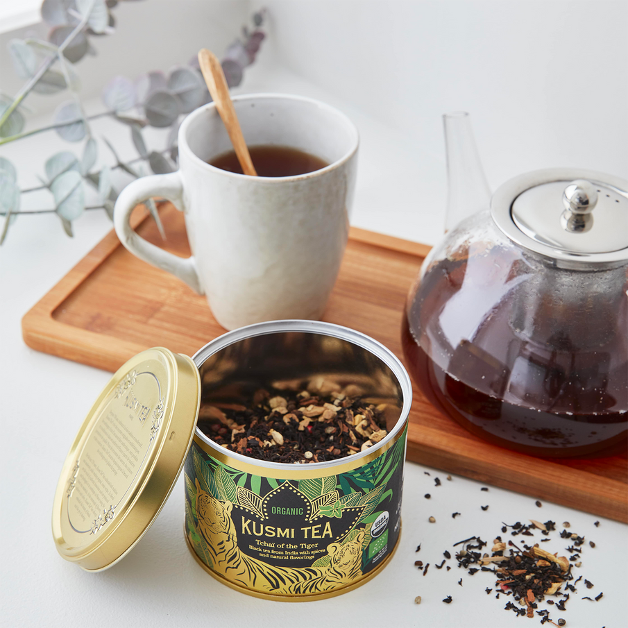 Boite de thé Kusmi Tea Tchaï of the Tiger ouverte, tasse et théière posées sur un plateau en bois