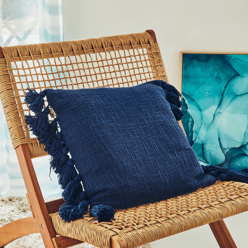 Coussin bleu à pompons posé sur une chaise en rotin