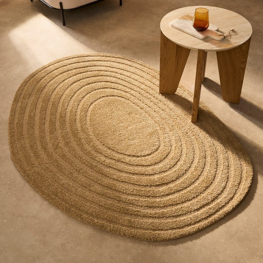 Tapis beige sable forme ovale aux motifs circulaires réguliers, table basse en bois et travertin