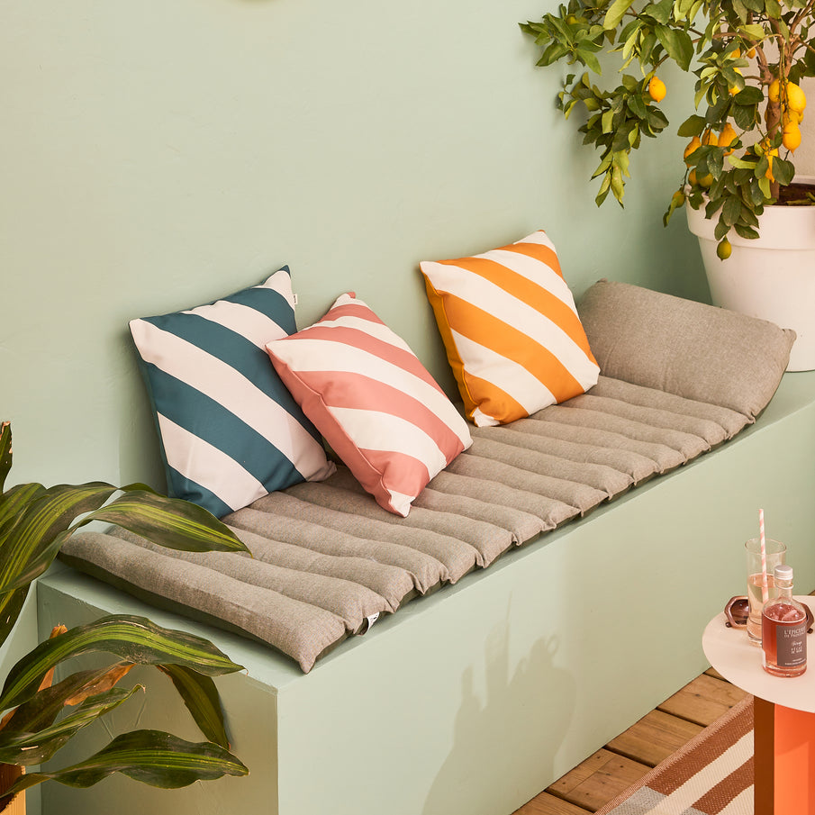 Ambiance terrasse avec banquette, coussins rayés, mur vert sauge et plantes