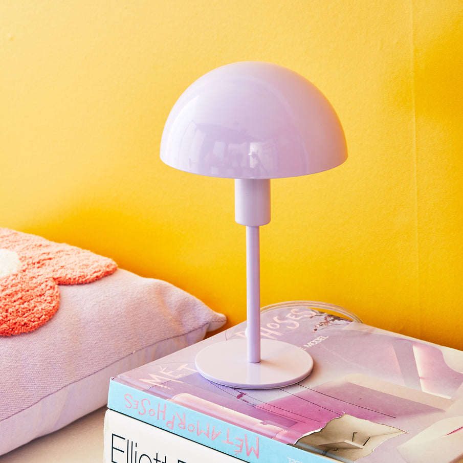 Lampe champignon violet posée sur des livres devant un mur jaune