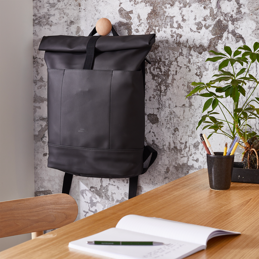 Sac à dos noir accroché à un mur effet pierre, à côté d'un espace de télétravail