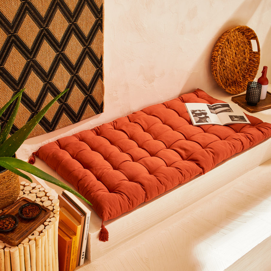 Banquette avec coussin de sol orange sur une terrasse style nomade