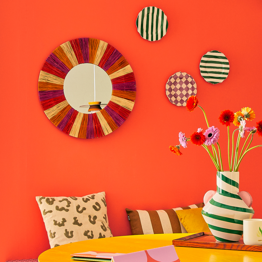 Mur peint en orange avec déco murale, coussins et vases rayés et colorés