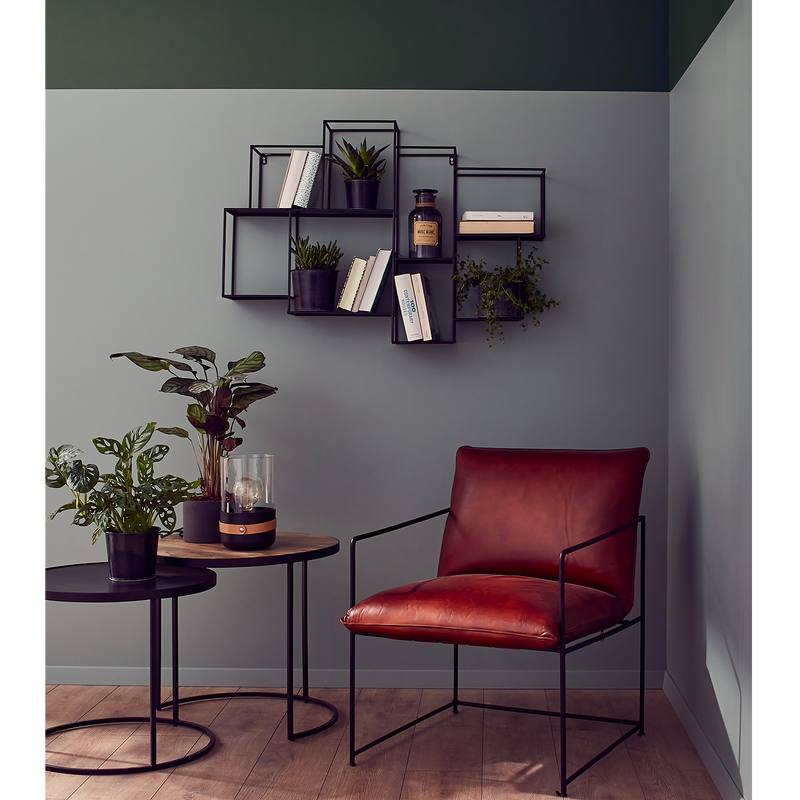 Salon casual en camaïeu vert avec fauteuil en cuir, tables basses et étagère métalliques et plantes vertes