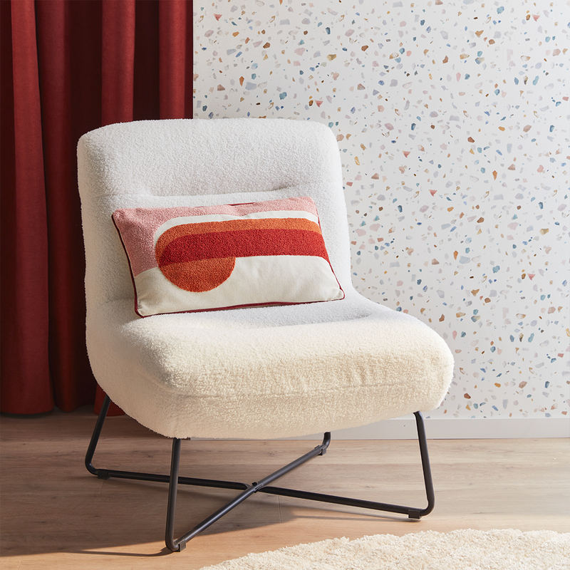 Fauteuil blanc à bouclette avec coussin rose-orange devant papier peint terrazzo et rideau rouge