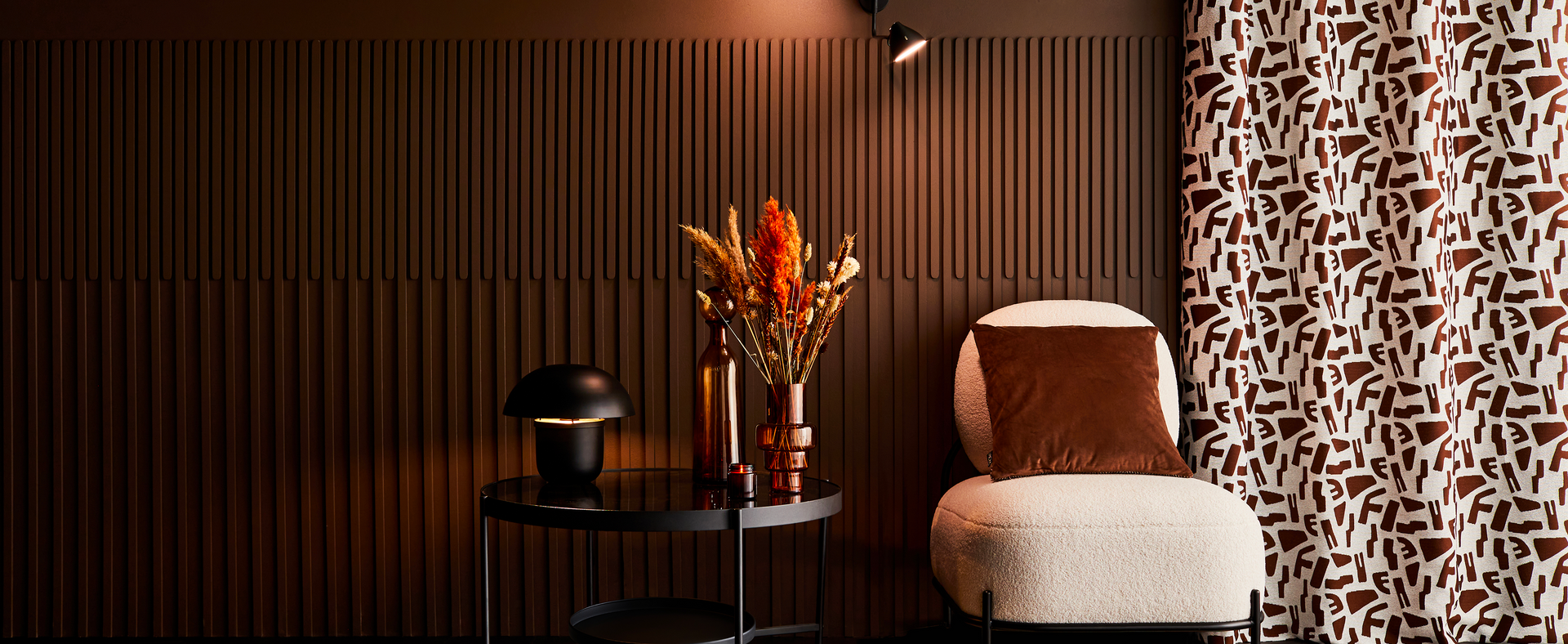 Salon brun avec un fauteuil blanc, devant un mur à reliefs et rideau à motifs abstraits
