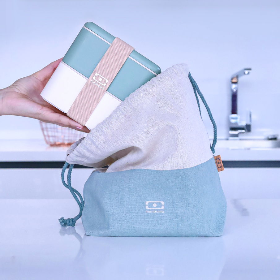 Main déposant une boite repas carré blanc et vert de la marque Monbento dans un sac de transport