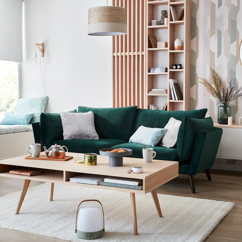 Salon avec canapé vert forêt, meubles en bois et tapis beige