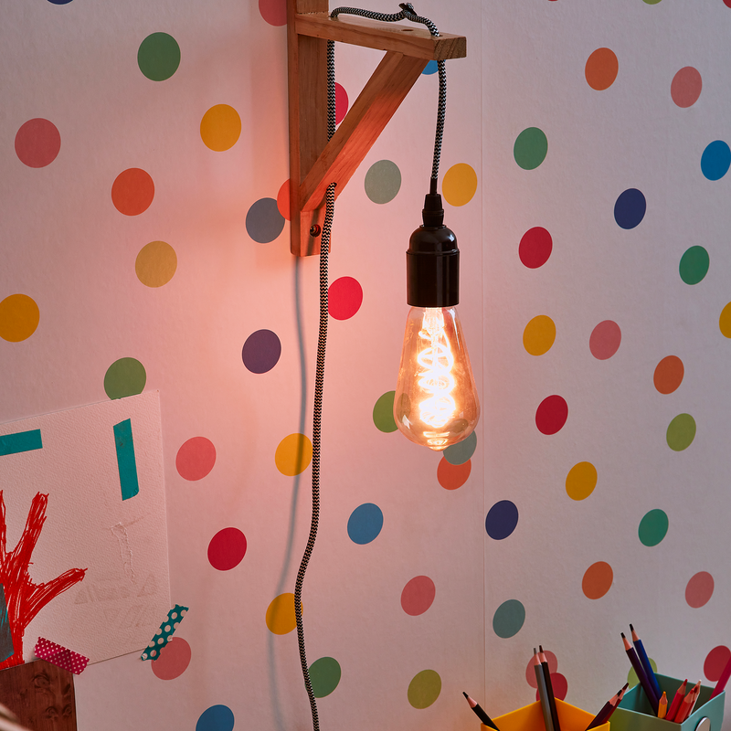 Applique avec ampoule allumé, accrochée  à un mur avec papier peint blanc à points multicolores