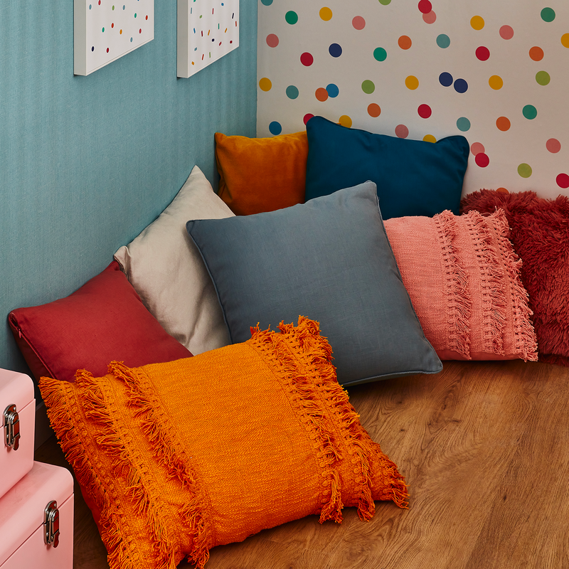 Coussins avec différentes textures et couleurs posés dans un coin au sol