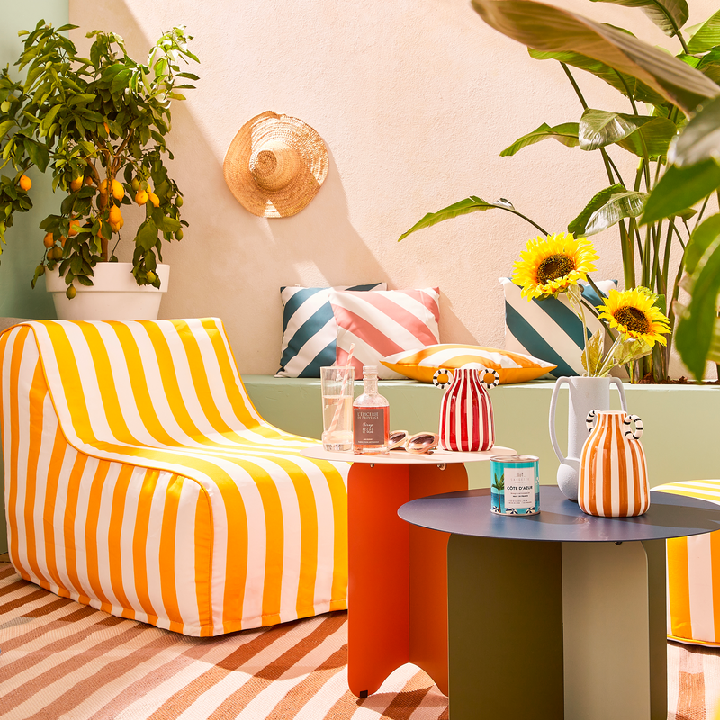 Chauffeuse, coussins, tapis et vases à rayures dans ambiance de terrasse solaire