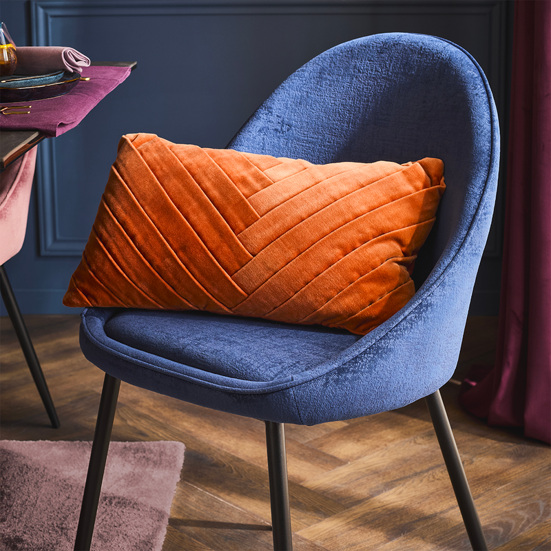 Coussin velours orange posé sur une chaise en velours bleu enveloppante
