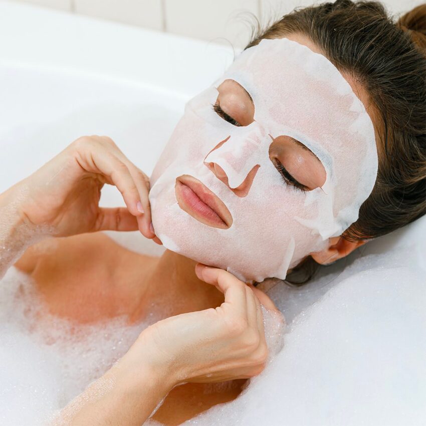 Femme avec soin visage masque en tissu dans un bain