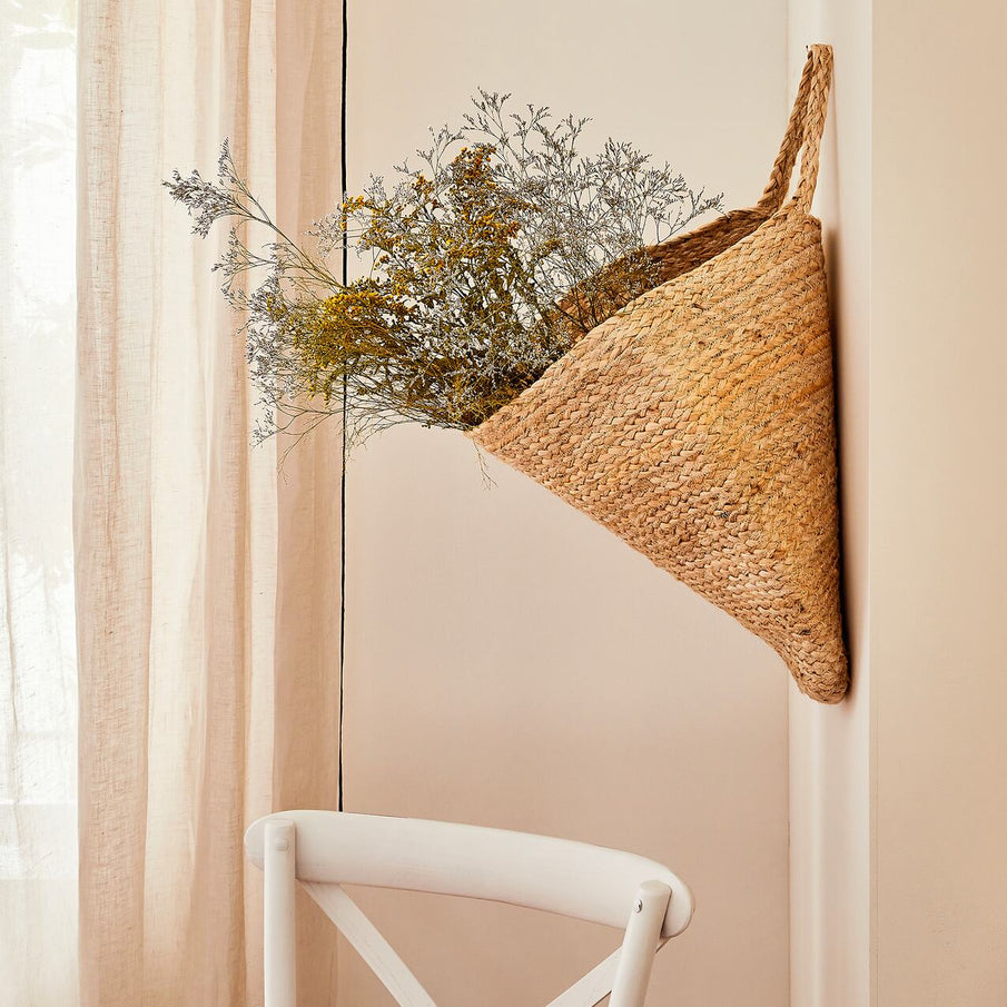 Panier tressé contenant des fleurs séchées accroché à un mur beige