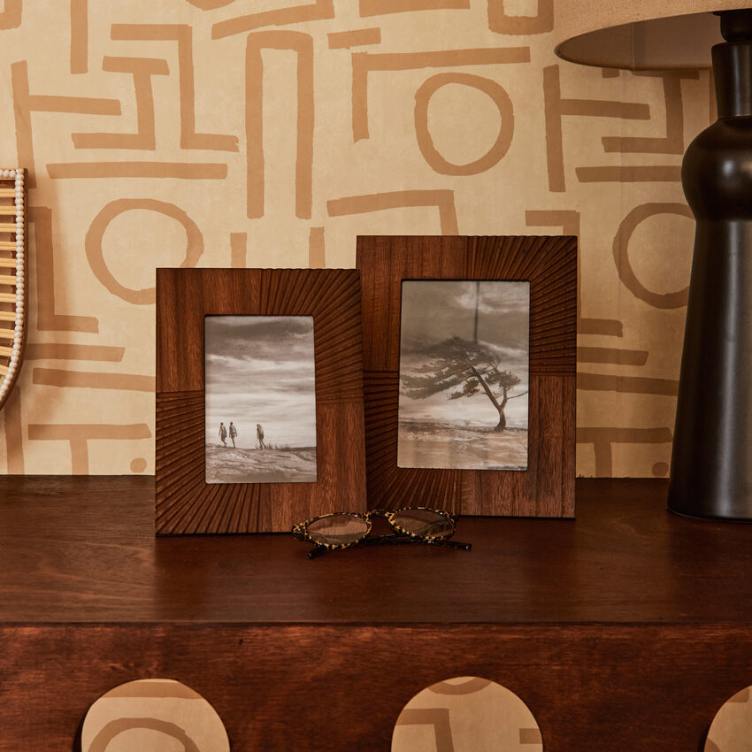 Deux cadres photos en bois foncé posés sur buffet, papier peint beige avec signes abstraits
