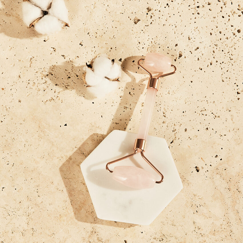 Roller visage quartz posé sur une pierre, sur fond beige