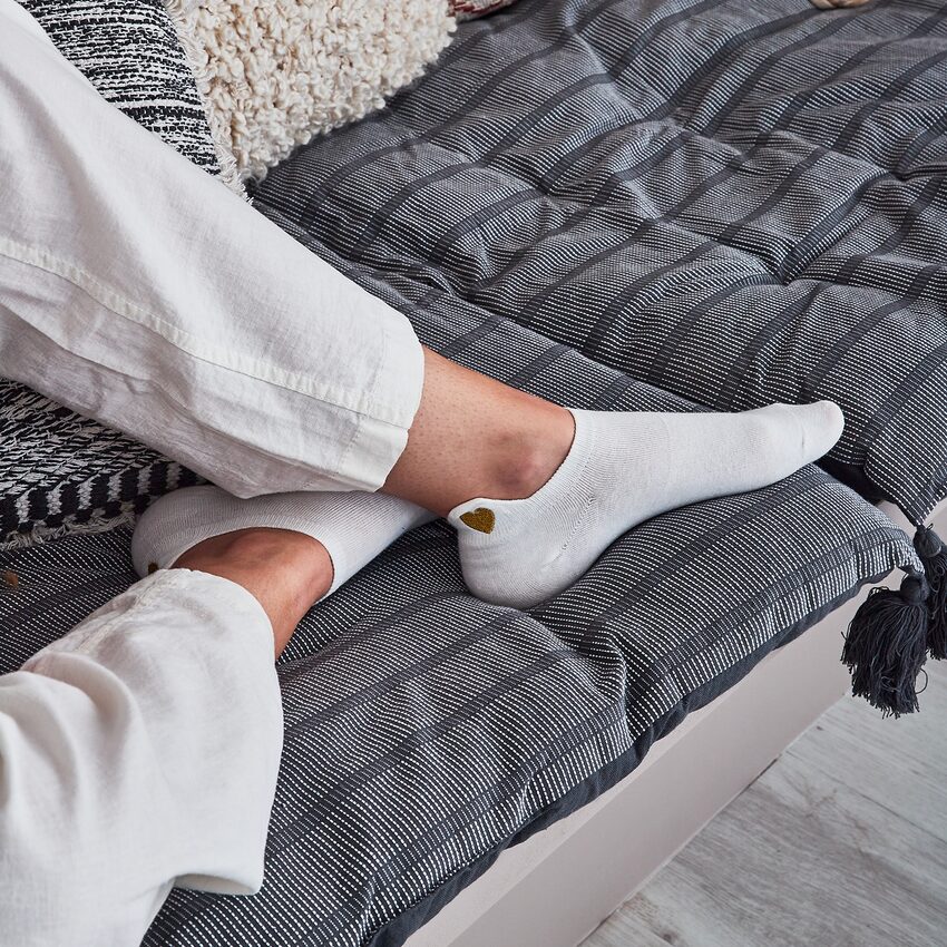 Chaussettes blanches avec cœur doré, pieds posés sur banquette avec coussins gris