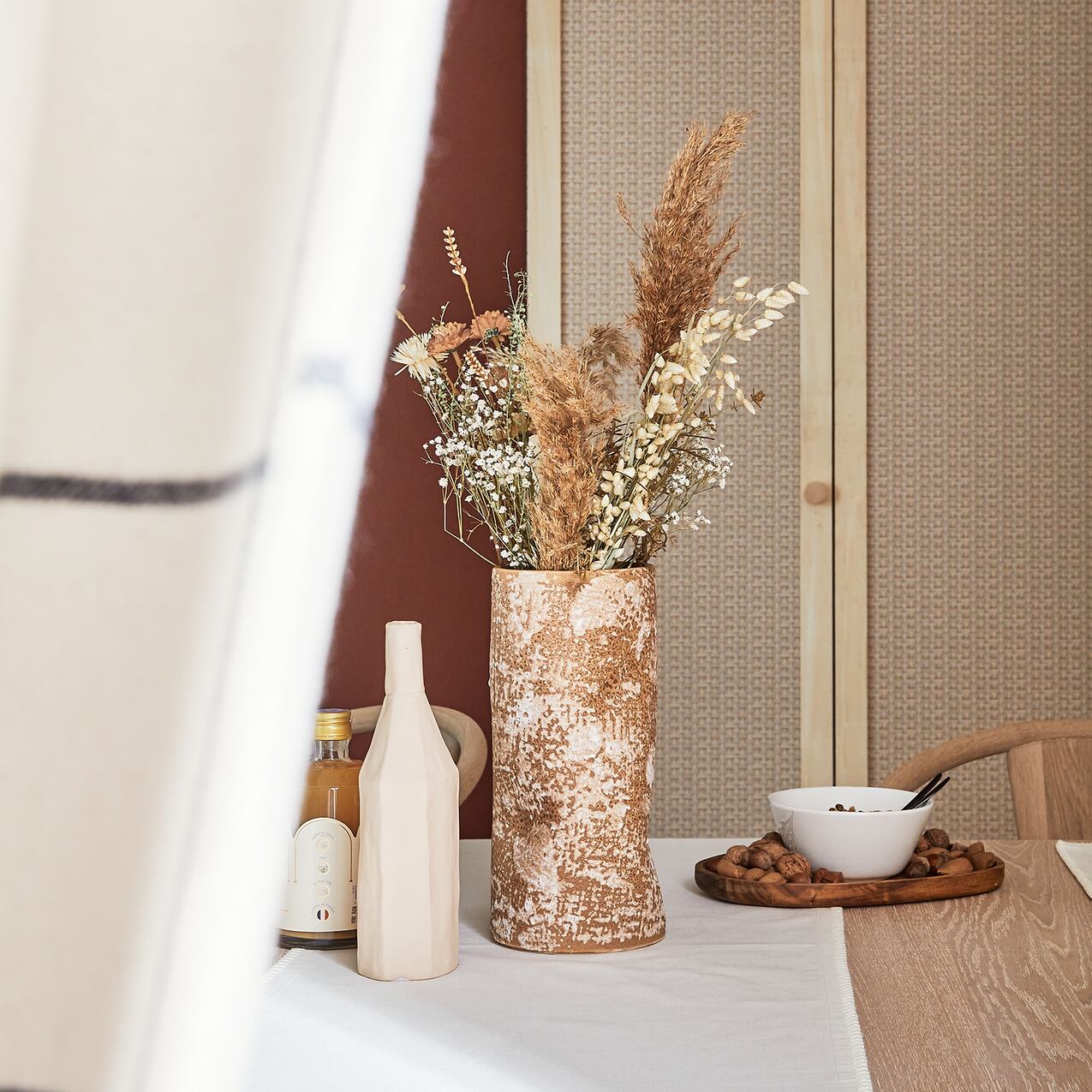 Vase en céramique rempli de fleurs séchées posé sur une table en bois clair