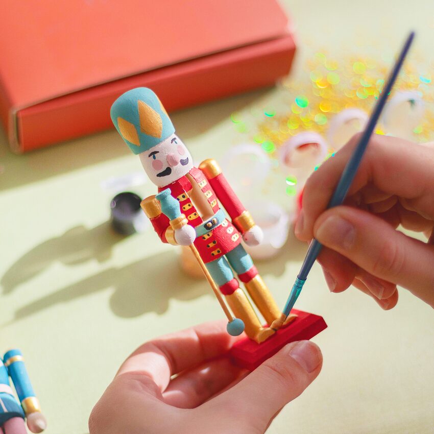 Une main tient un pinceau pour peindre un Casse-Noisette tenu par l'autre main