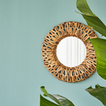 Miroir rond au cadre de plantes séchées tressées accroché à un mur bleu ciel