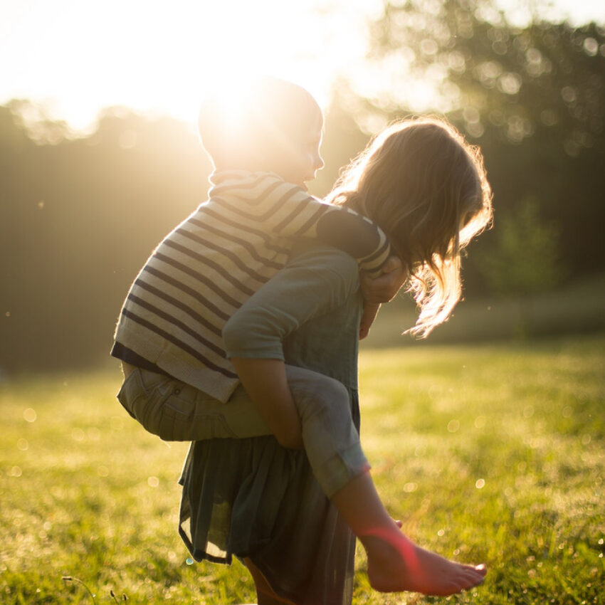 Fille portant un garçon sur son dos dans un champs au soleil couchant