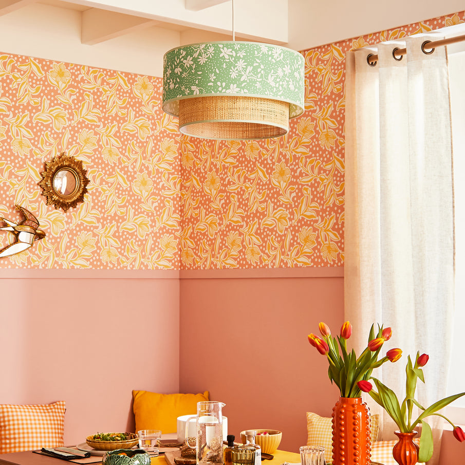 Coin repas coloré à la peinture rose et au papier peint fleuri aux couleurs rose et jaune, suspension fleurie également de couleur verte, décoration murale dorée, rideaux blancs