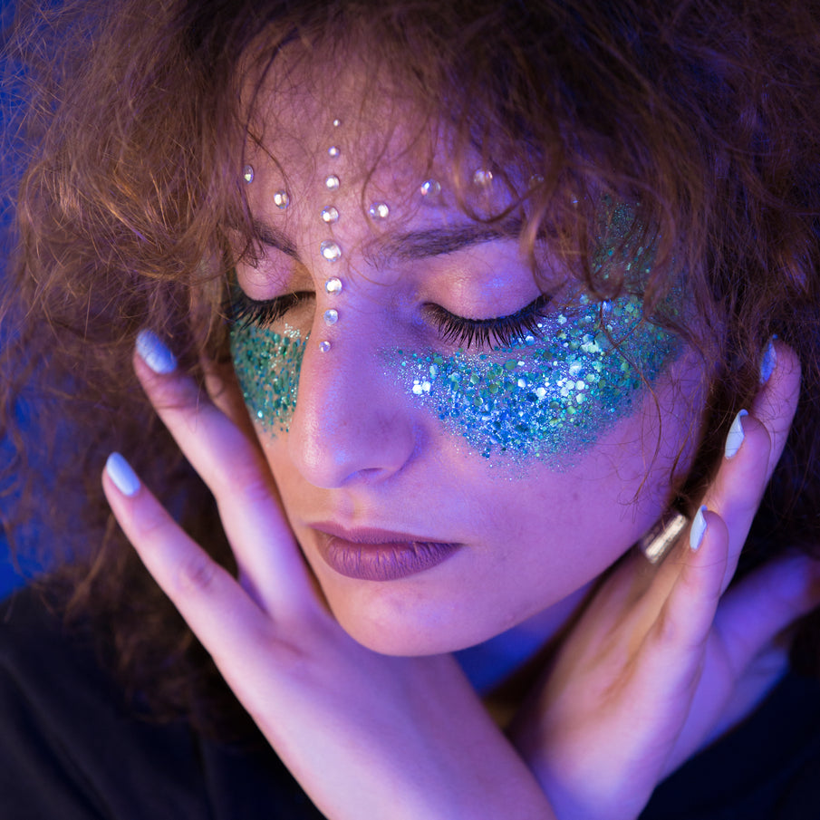 Visage de femme paupières fermées, maquillée avec des paillettes bleu vert sur les pommettes
