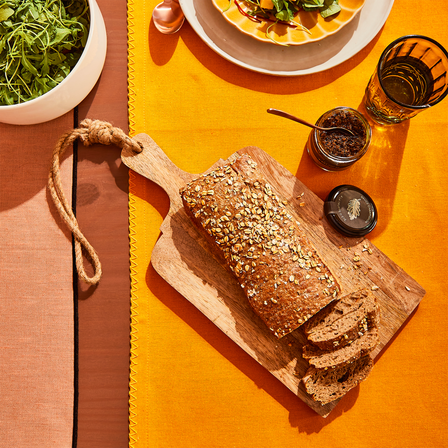 Pain, pot à tartinade et planche à découper posés un chemin de table jaune 