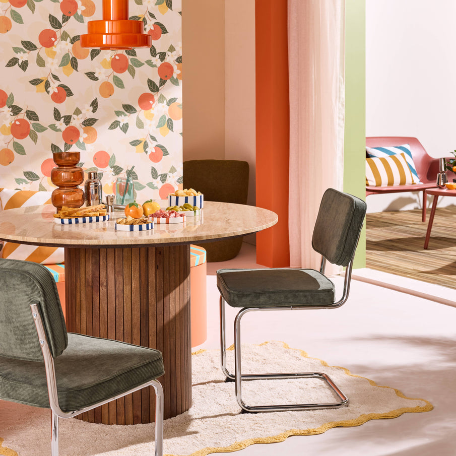 Salle à manger avec table ronde en marbre et chaises en velours vert, papier peint à motifs agrumes