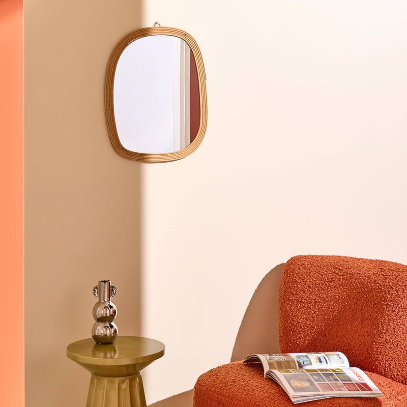 Miroir rectangulaire en bois aux bord arrondis, fauteuil couleur terracotta tissu bouclette, vase chromé posé sur un bout de canapé