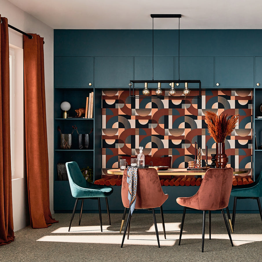 Salle à manger aux couleurs rouille et bleu paon, chaises en velours, papier peint au motif géométriques abstraits, banquette intégrée au mur 