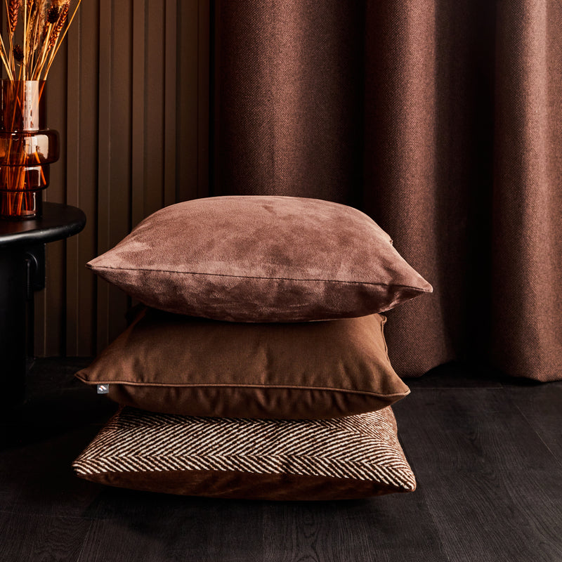 Trois coussins en velours bruns empilé au sol devant rideau et mur bruns