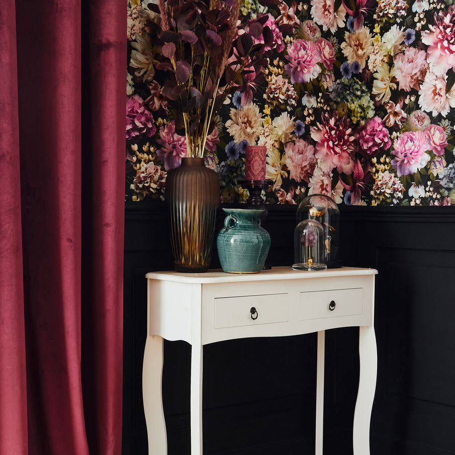Papier peint motif fleuri, rideau velours rouge bordeaux et vases posés sur une console en bois blanc