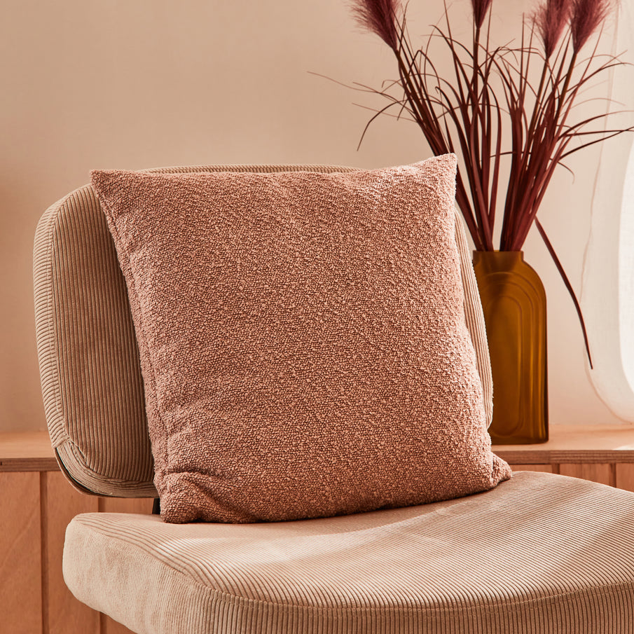 coussin rose en tissu bouclette sur un fauteuil en velours côtelé beige