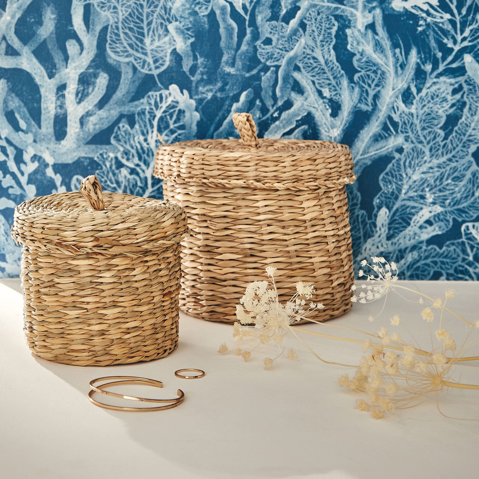 2 paniers tressés et fleurs séchées devant papier peint bleu à motif coraux blancs