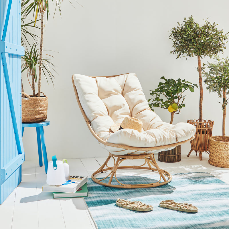 Fauteuil en osier avec coussin mœlleux sur tapis extérieur installés en terrasse