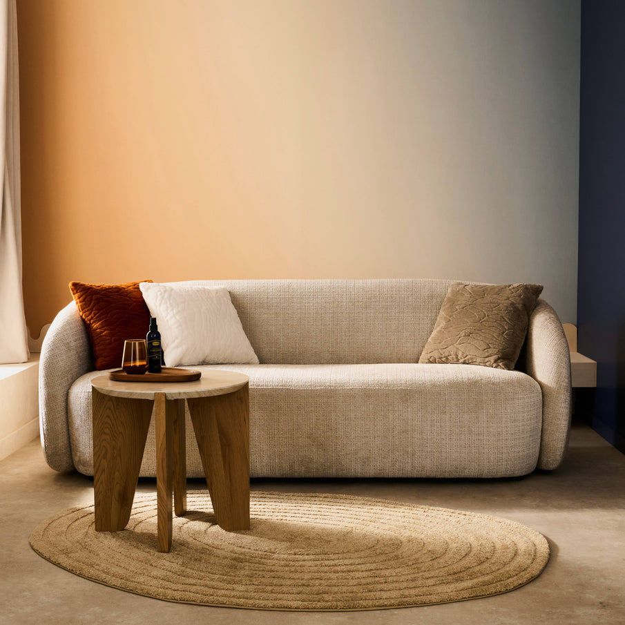 Canapé tissu beige bords arrondis, tapis beige circulaire, papier peint dégradé orange et bleu