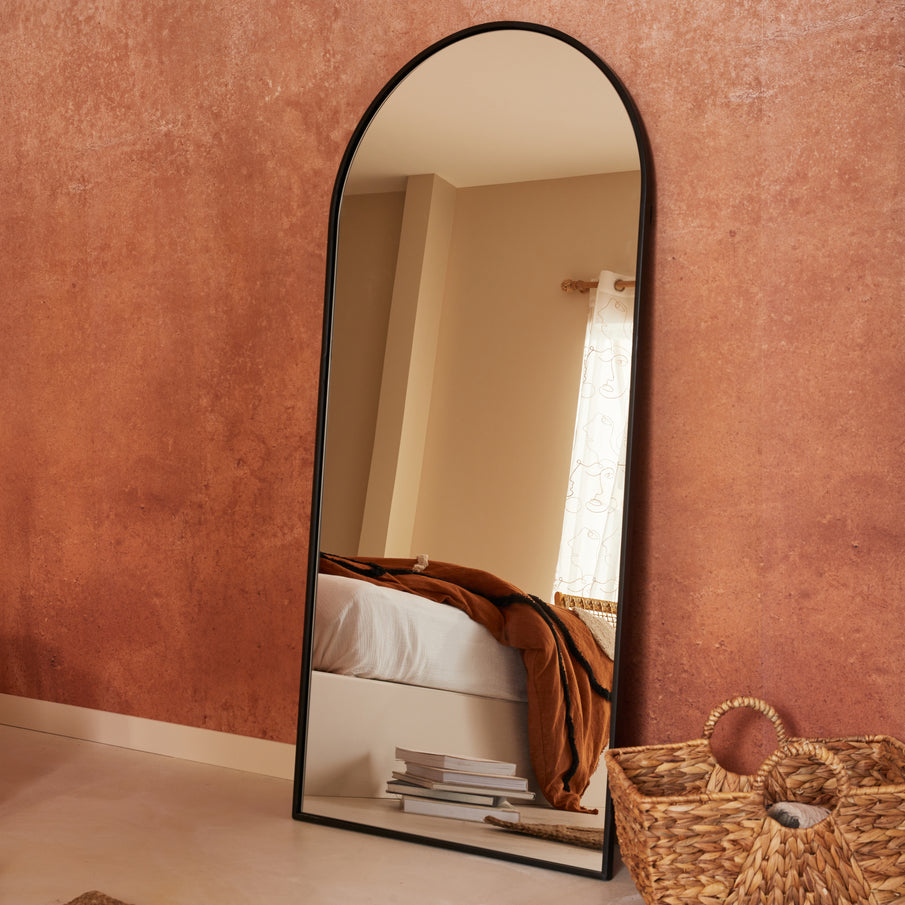 Grand miroir au cadre noir en forme d'alcôve posé au sol dans une chambre couleur terracotta
