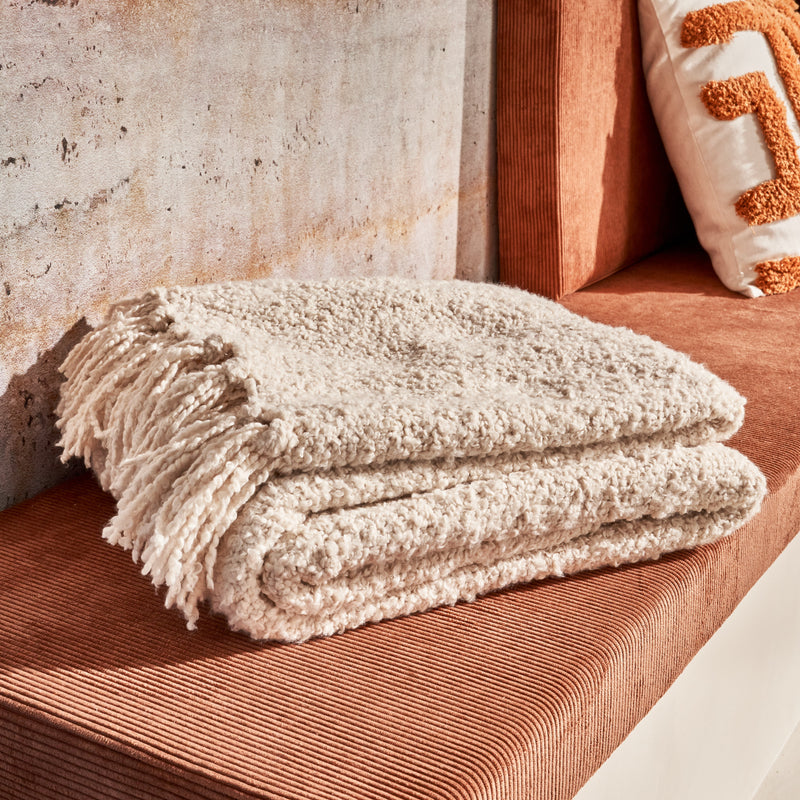 Plaid en laine bouclée pliée sur une banquette en velours côtelé