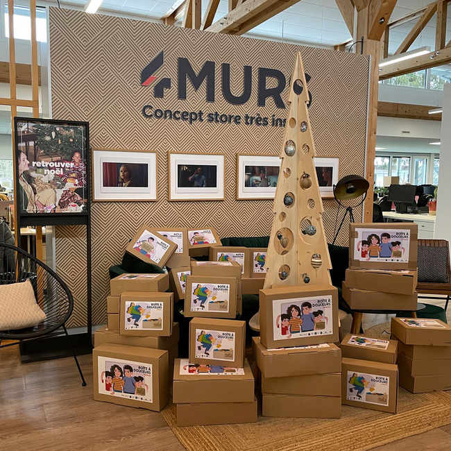 Boites en carton empilées au pied d'un sapin figuratif en bois dans l'entreprise 4MURS, boites à douceurs solidaires