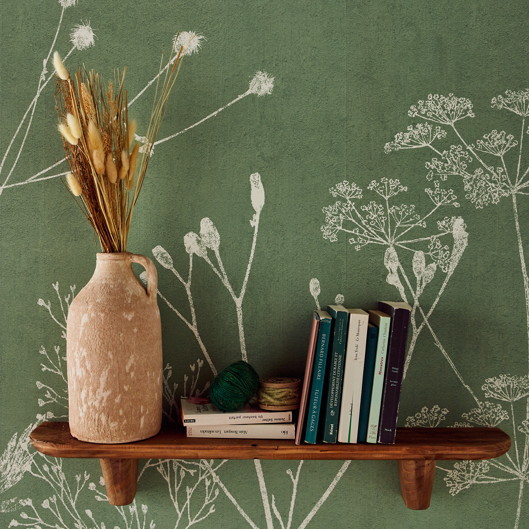 Étagère en bois avec livres et vase sur papier peint vert à motif floral blanc
