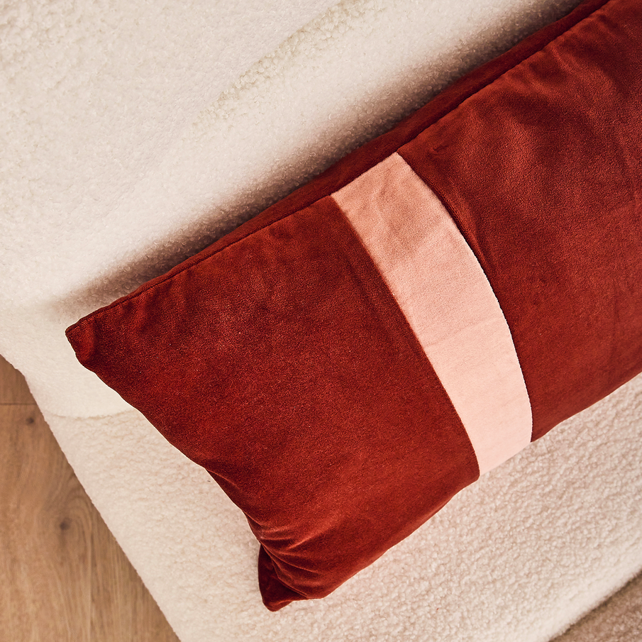 Coussin velours rouge posé sur un fauteuil blanc au tissu bouclette